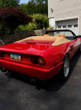 Red convertible sports car parked in a driveway beside a house, with tan interior and top down