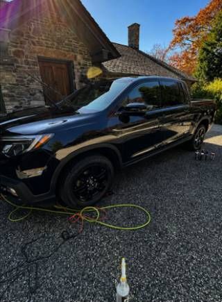 Black SUV parked on gravel beside a stone house, with a hose and bottle in the foreground.