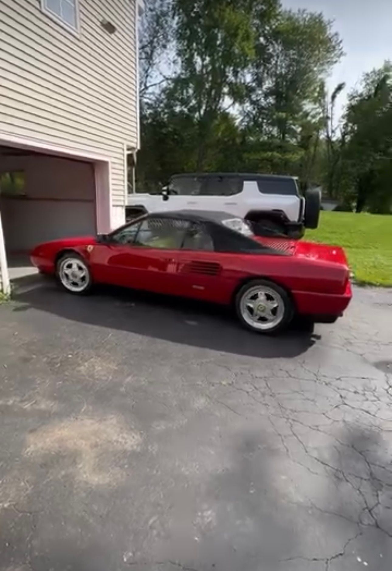 Red convertible parked in a driveway beside a garage, with a white SUV behind it.