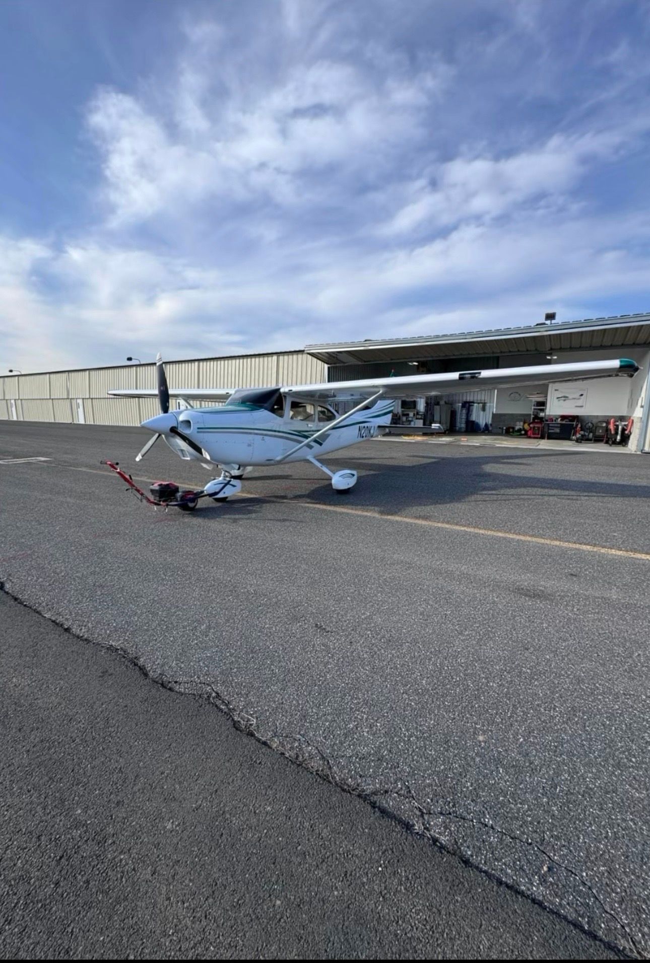 Small blue-and-white airplane parked on an airport tarmac near a hangar under a cloudy sky