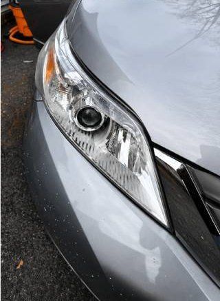 Close-up of a silver car’s front headlight and grille, with a small scuff on the bumper.