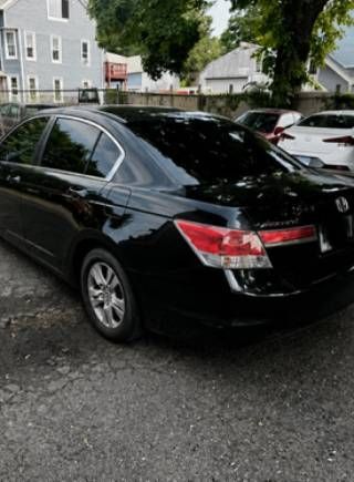 Black sedan parked in a lot beside houses and trees