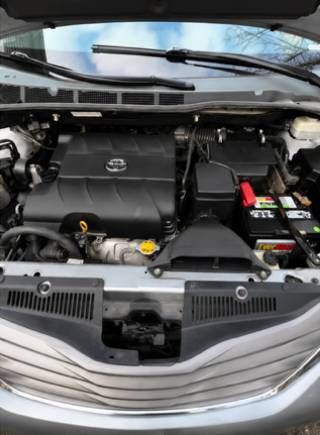 Car engine bay with black cover, visible battery, hoses, and windshield wipers above.