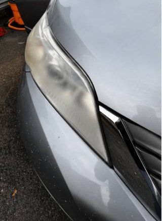 Close-up of a silver car’s front corner with a cracked headlight lens and damaged bumper area