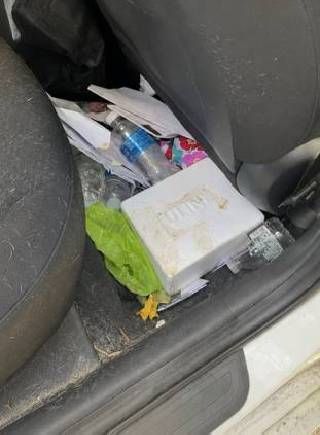 Cluttered car back seat with a water bottle, tissues, and a box on the floor.
