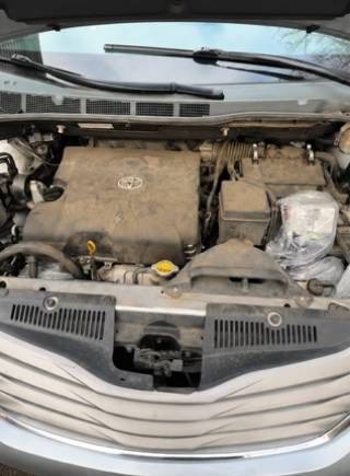 Car engine bay with dusty engine cover and visible components under an open hood