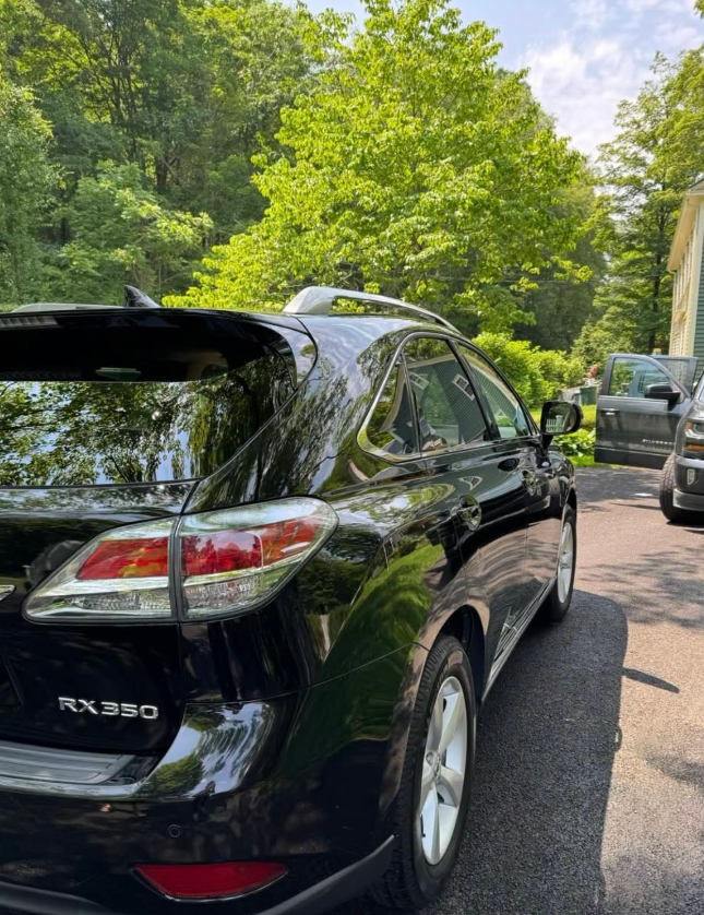 A black lexus rx350 is parked in a driveway with trees in the background.