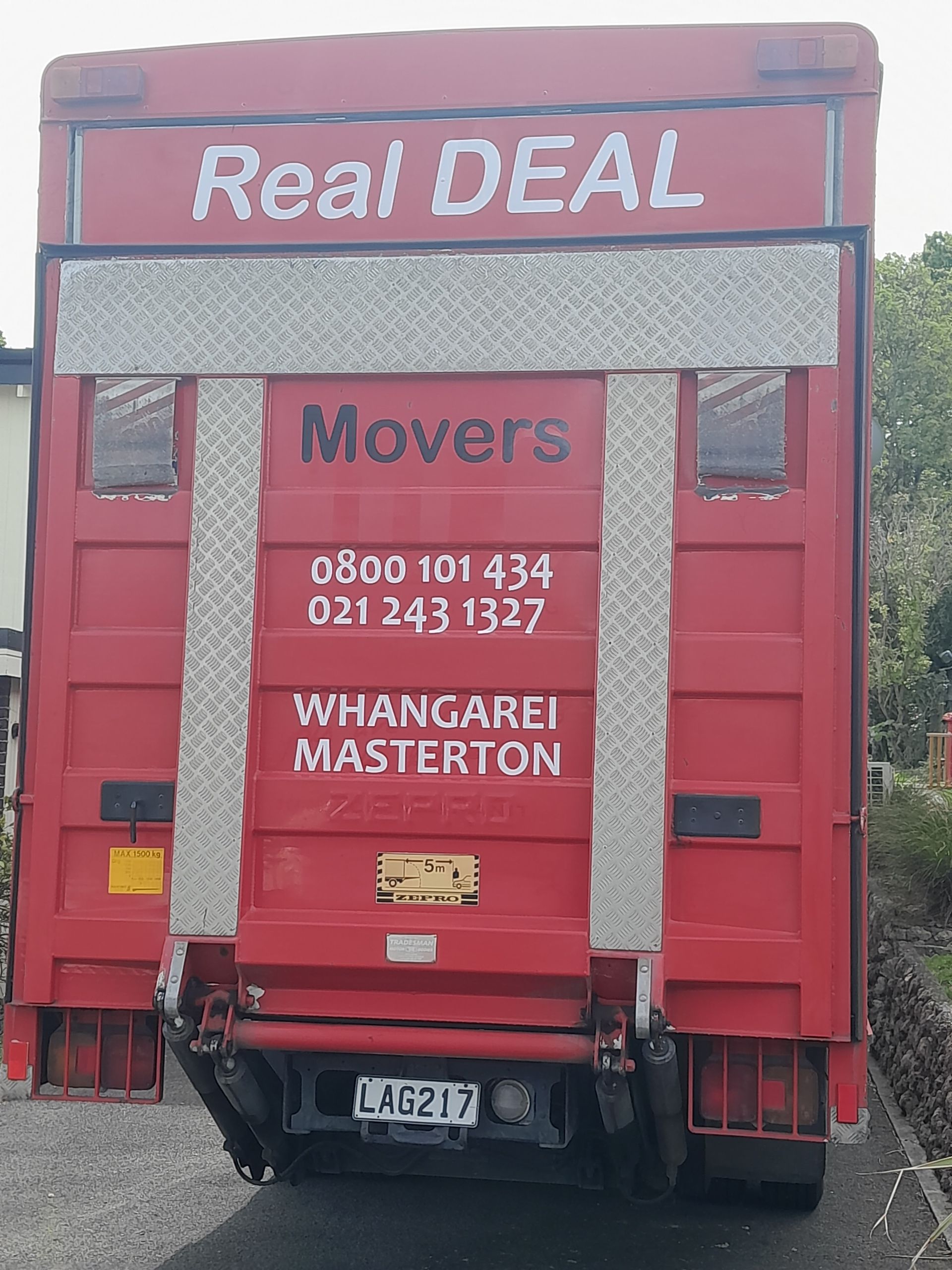 A Red Real Deal Movers truck is parked in a driveway.