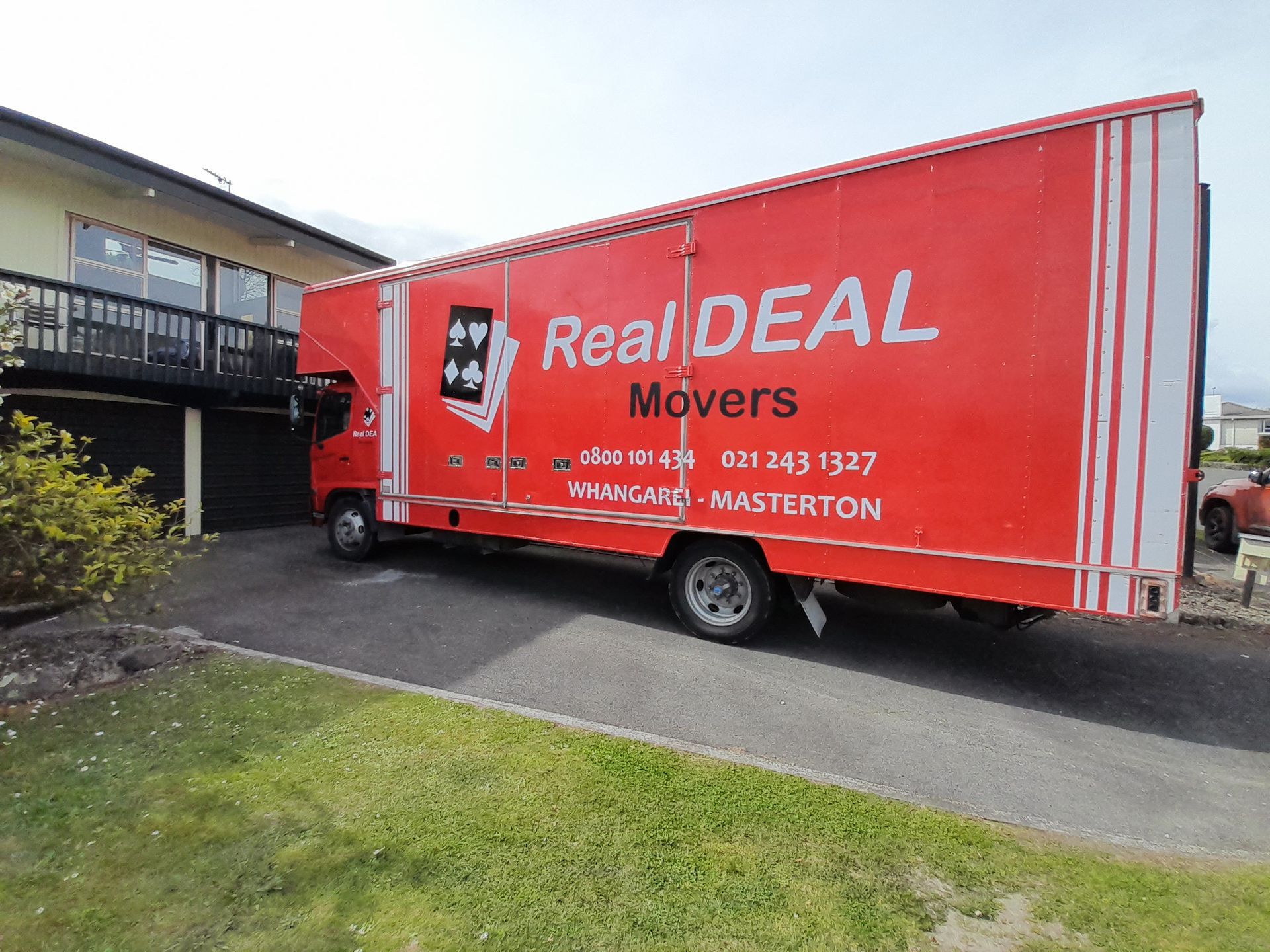 A red Real Deal Movers truck is parked in front of a house.