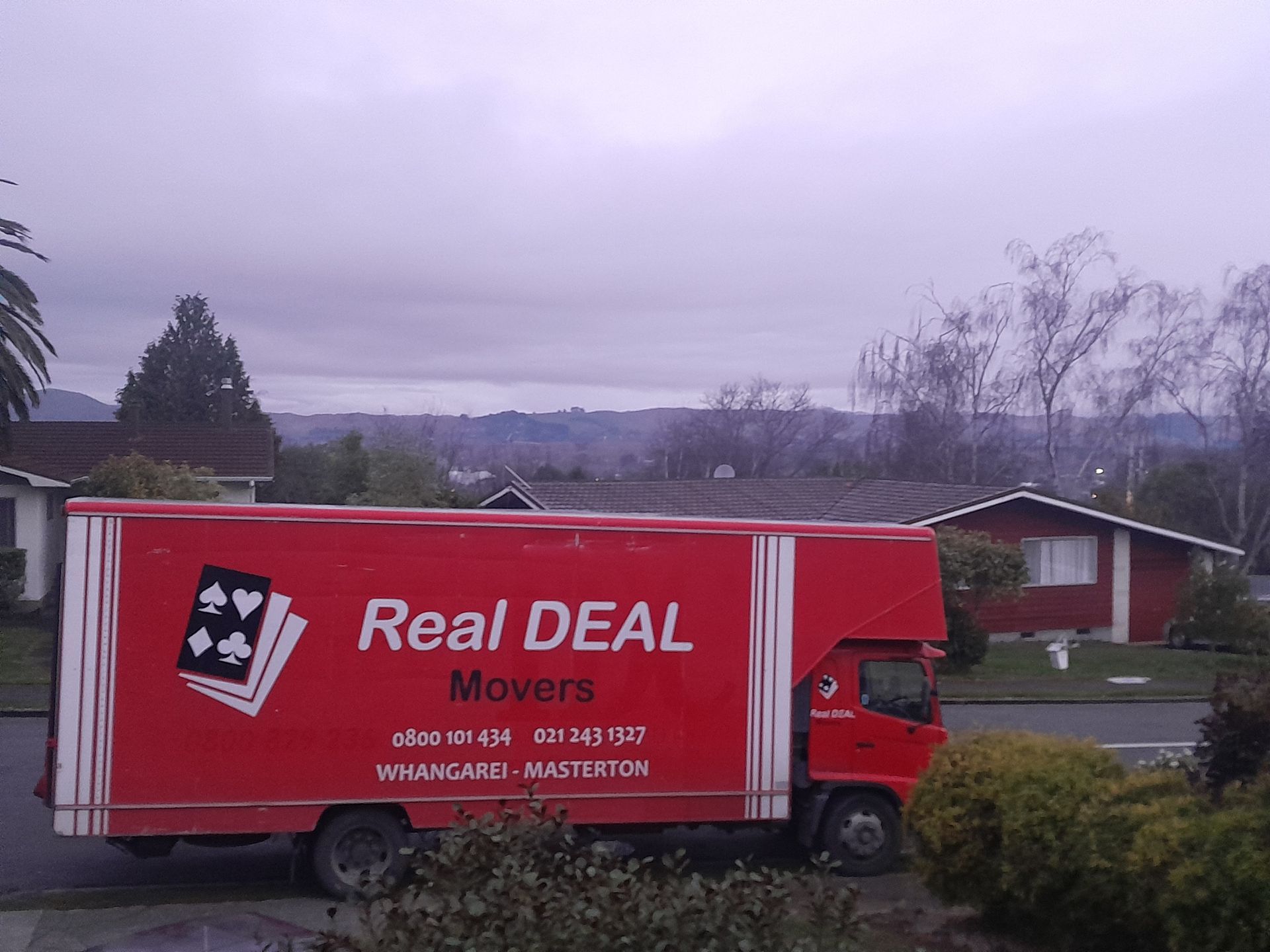 A Red Real Deal movers truck is parked in front of a house.