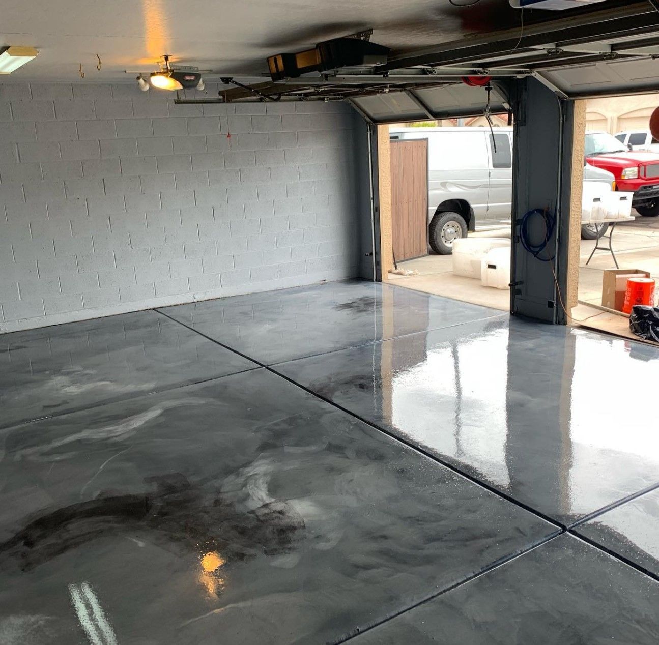 Empty garage with glossy wet concrete floor, open door, and reflections of a truck outside