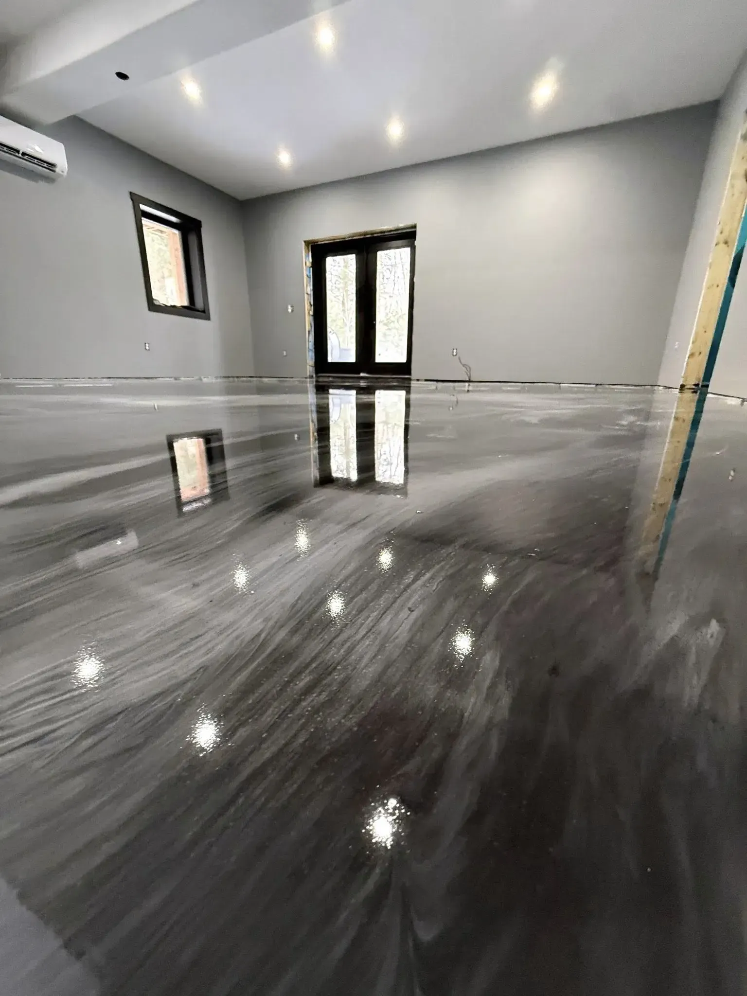 Empty modern room with glossy gray floor, white walls, and black-framed windows and door.