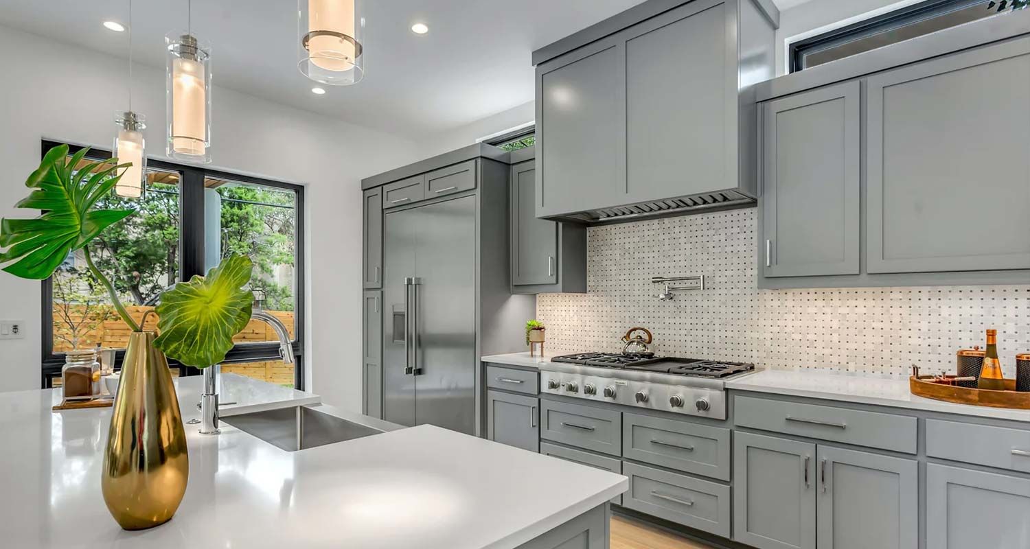 Bright modern kitchen with gray cabinets, white island, stainless appliances, and a vase of greenery