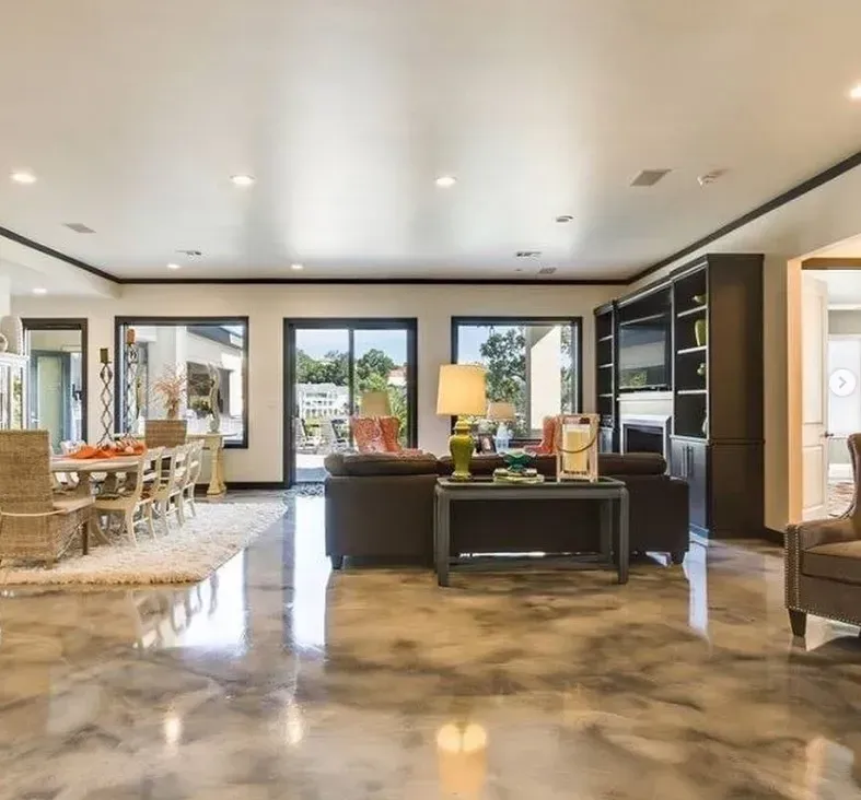 Open-plan living room with polished concrete floor, dark furniture, and large windows opening to a patio.