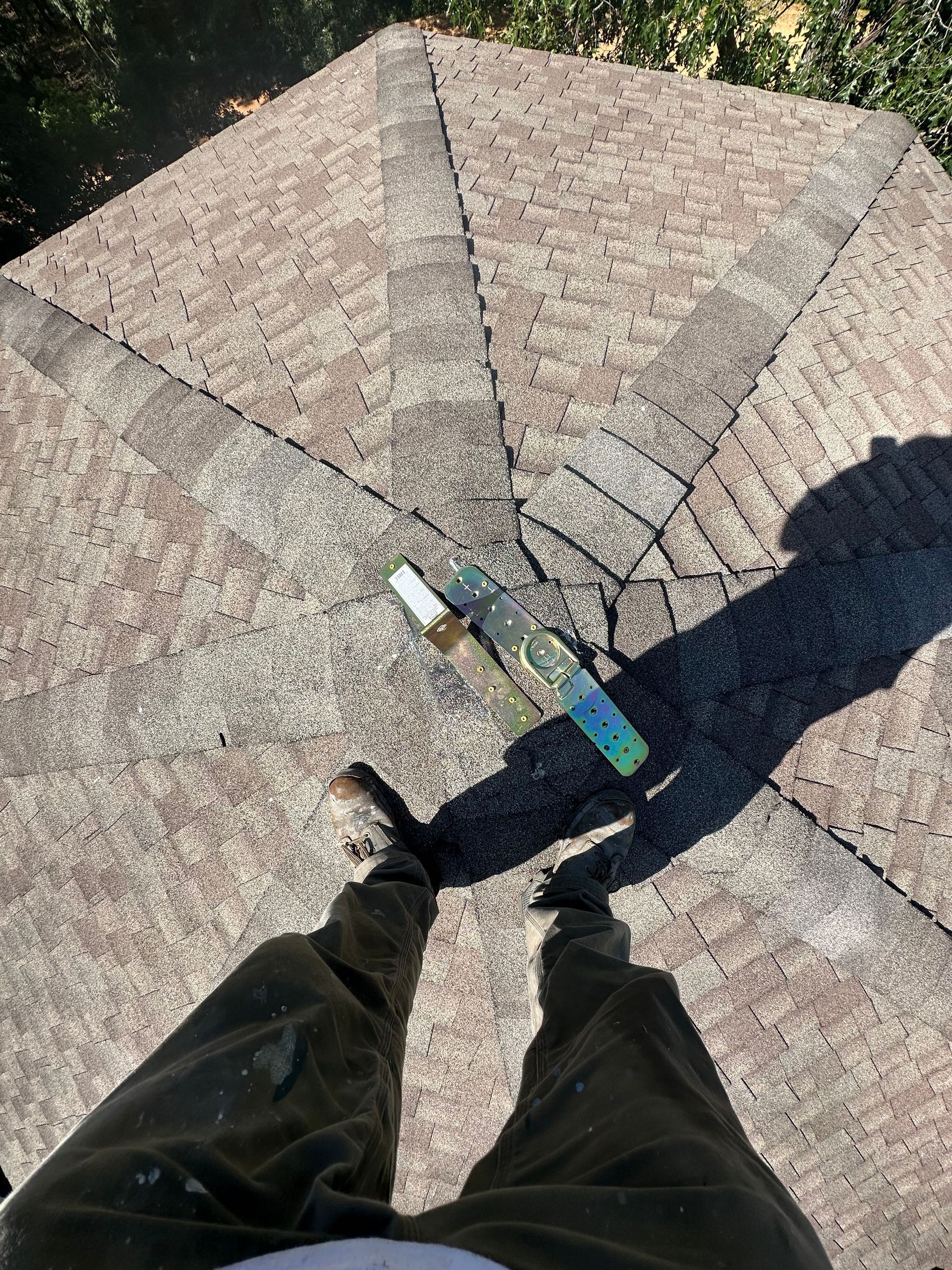 Looking down at legs and a colorful hammer on a shingled roof with a small crack nearby