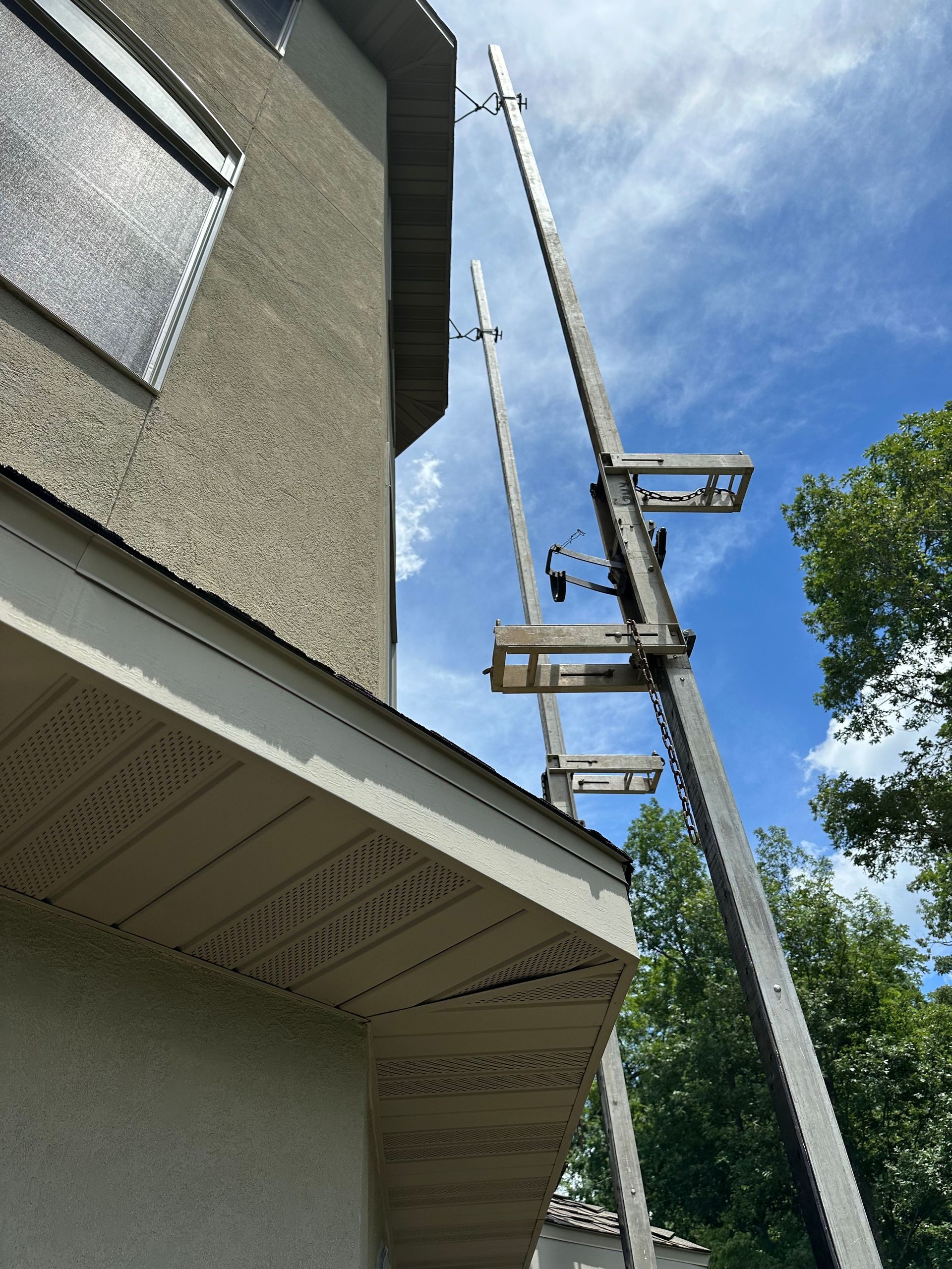 Two tall ladders leaning against a building beside a roofline under a blue sky.