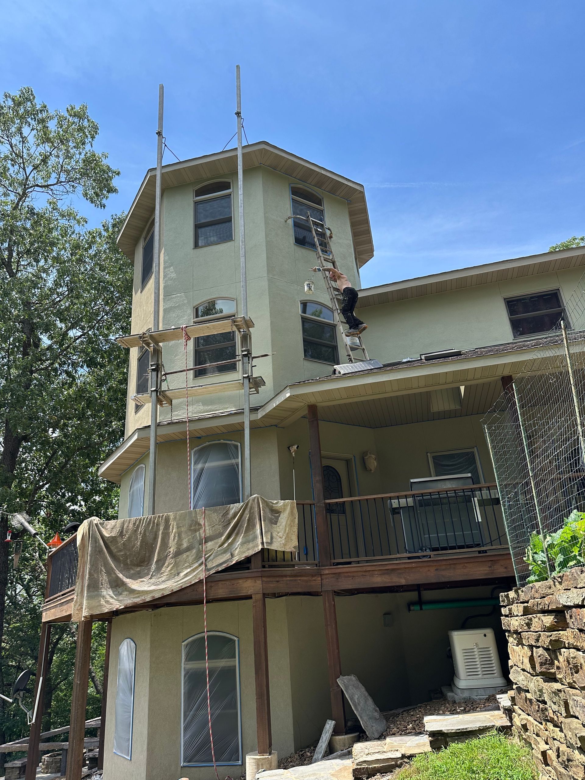 Multi-story house with scaffolding, covered porch, and stone steps under a clear blue sky