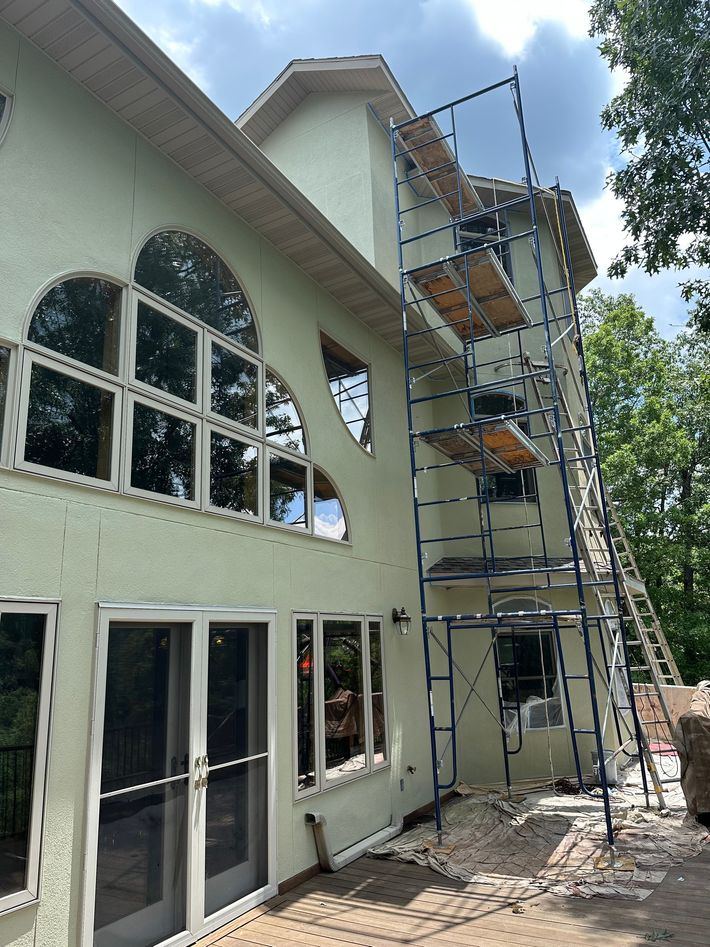 Two-story house exterior with scaffolding and ladders beside tall arched windows during construction