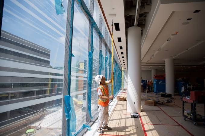 Worker in orange vest applying blue window film inside a bright building under construction