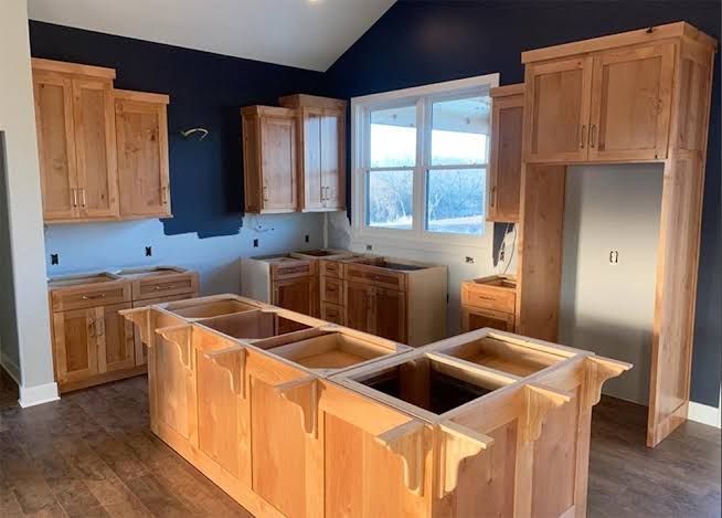 Unfinished kitchen with wooden cabinets, dark walls, island, and large windows.