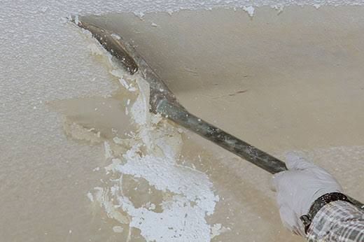 Person scraping peeling paint from a ceiling with a putty knife