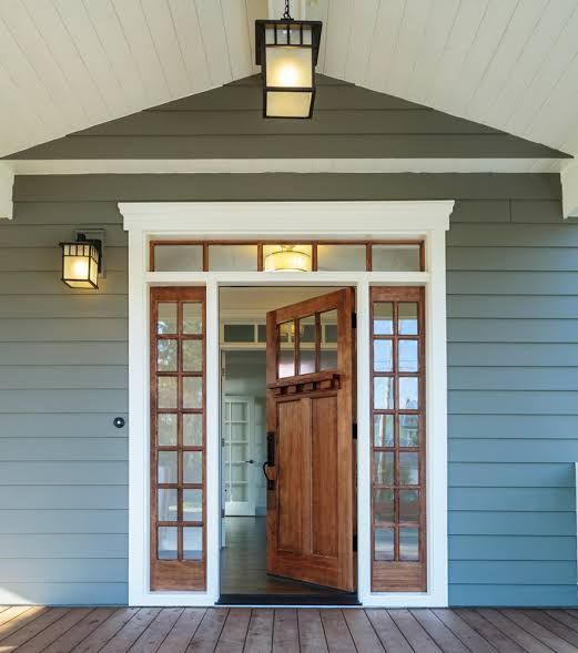 Front porch entrance with gray siding, white trim, and open wooden door under lantern lights