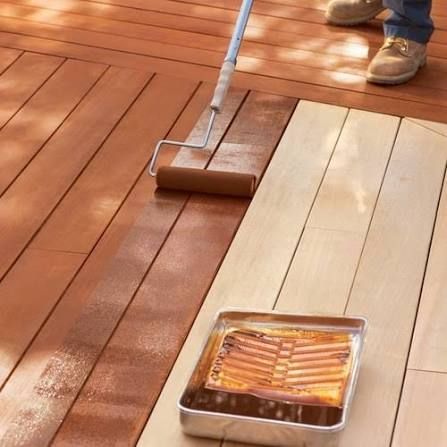 Person staining a wooden deck with a paint roller and tray of brown stain