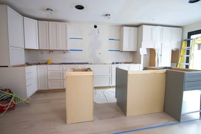 Unfinished kitchen with white cabinets, beige island, and work surfaces under renovation.