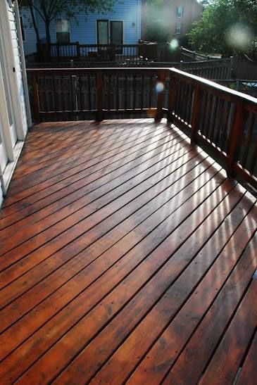 Wooden deck with rain-slicked boards and dark railing, overlooking a backyard at dusk