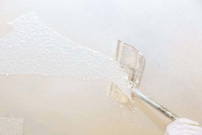 Person applying white paint to a textured wall with a putty knife