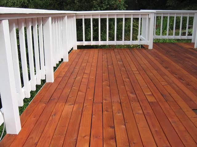 Wooden deck with reddish planks and white railings overlooking greenery