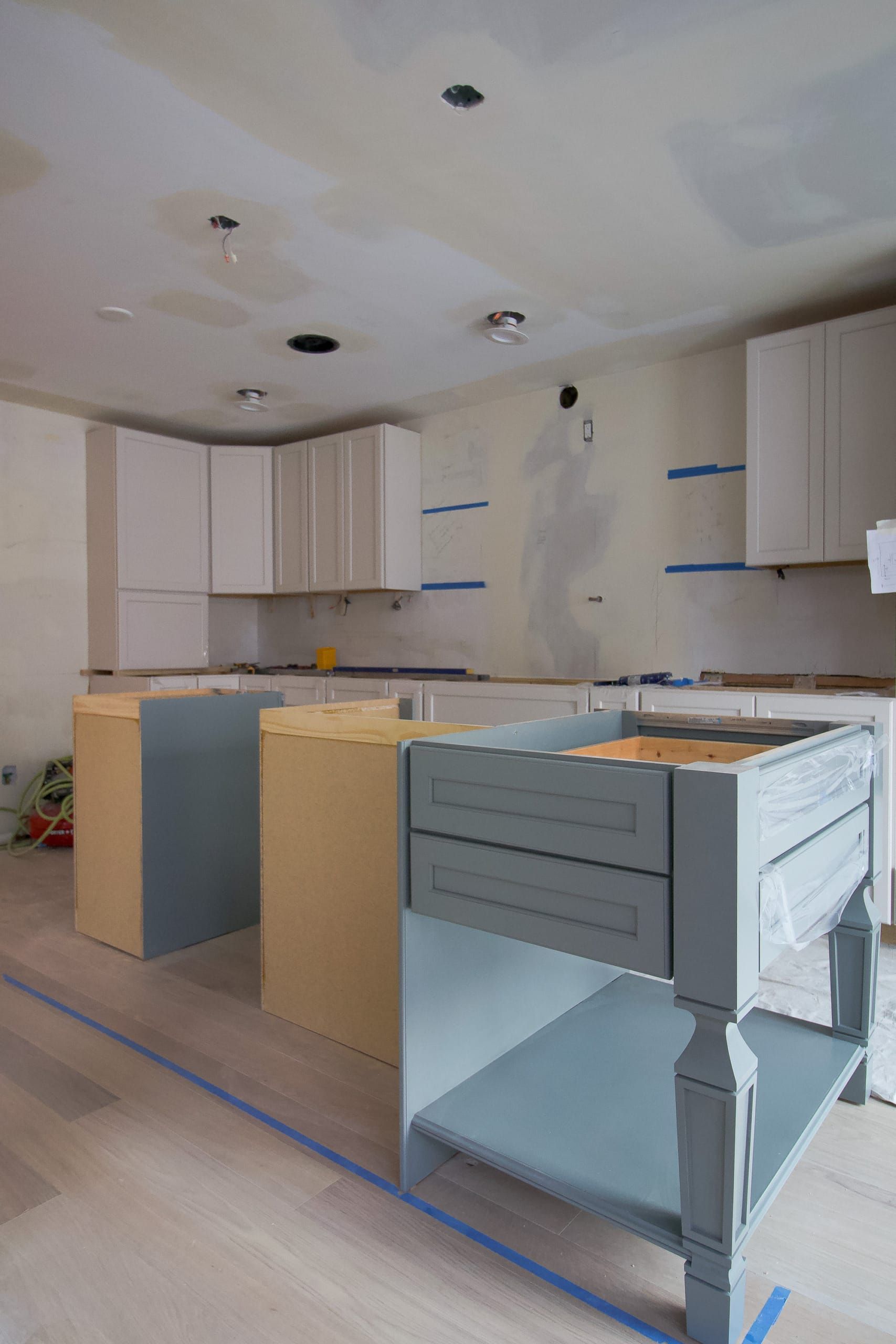 Unfinished kitchen with cabinets being installed, bare walls, and wrapped appliances on the floor.