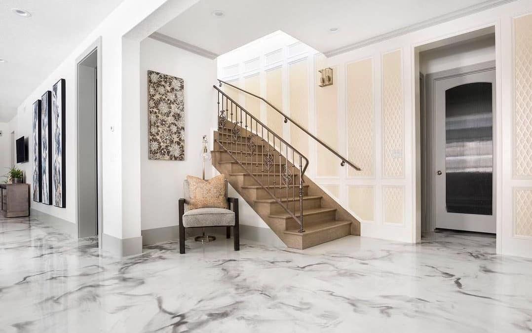 Bright marble foyer with a staircase, bench, framed art, and a dark doorway on the right