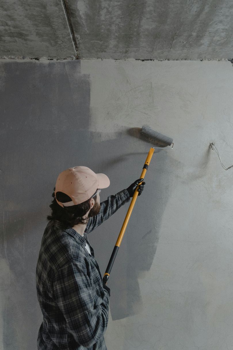 Person painting a gray wall with a roller on an extension pole.