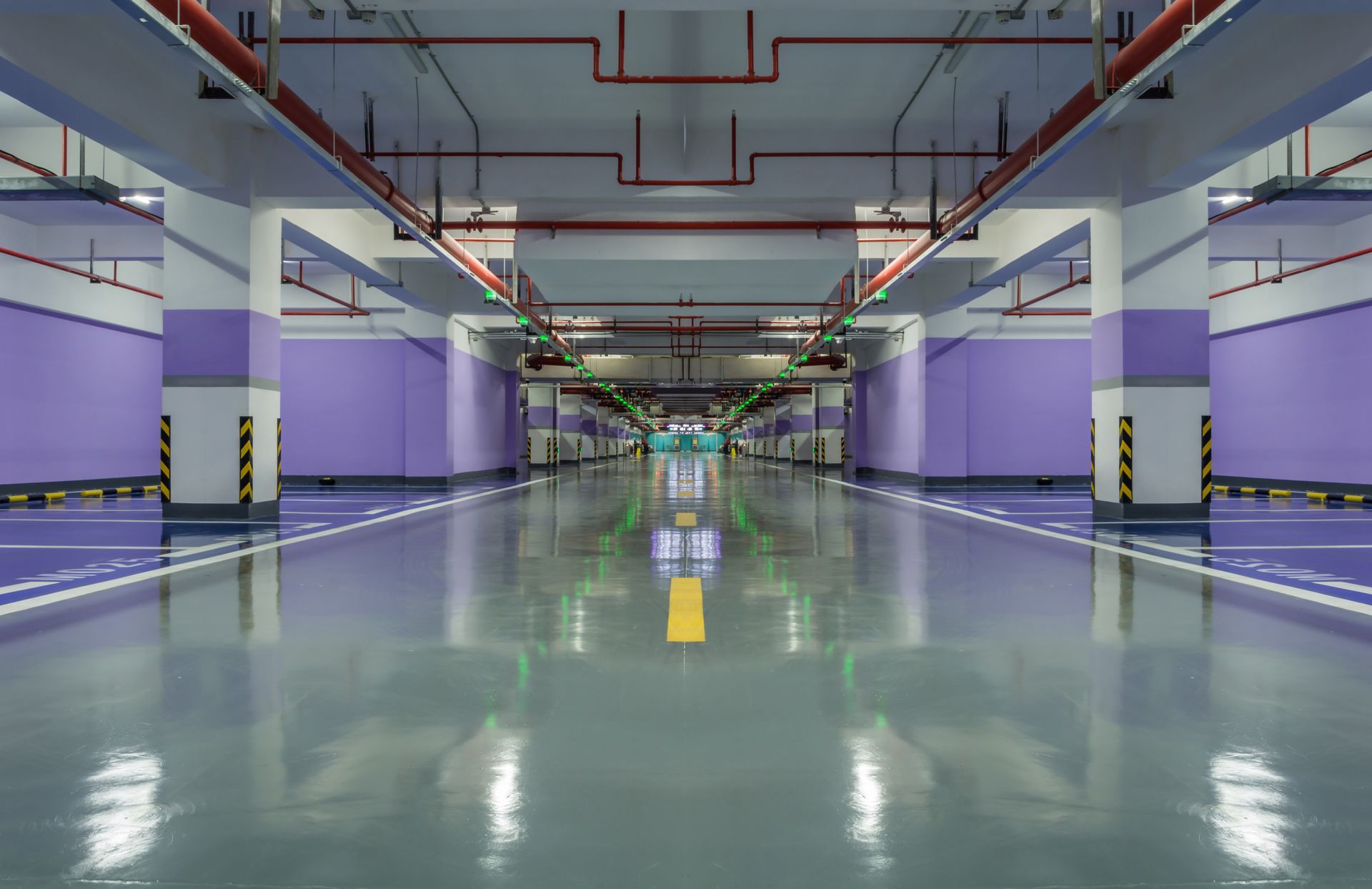 Empty underground parking garage with glossy floor, purple walls, and yellow-black striped pillars