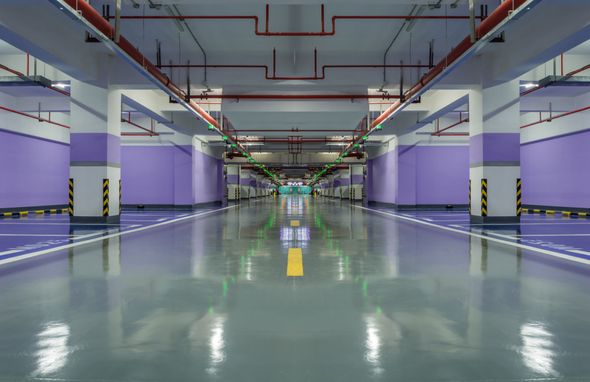 Empty underground parking garage with purple walls, polished floor, and overhead pipes