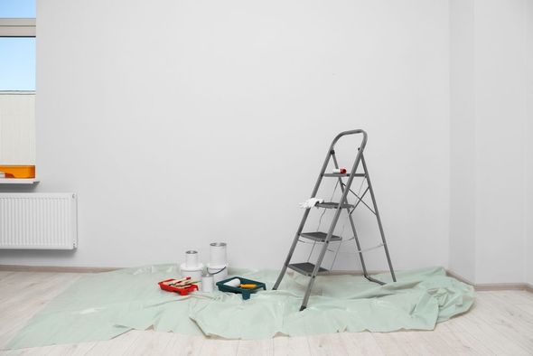 Empty room with ladder, paint supplies, and drop cloths, suggesting renovation work