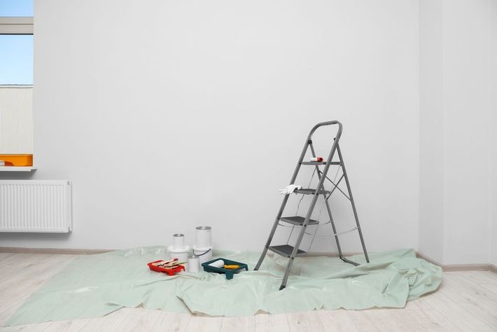 Empty room with ladder, paint supplies, and drop cloths, suggesting renovation work