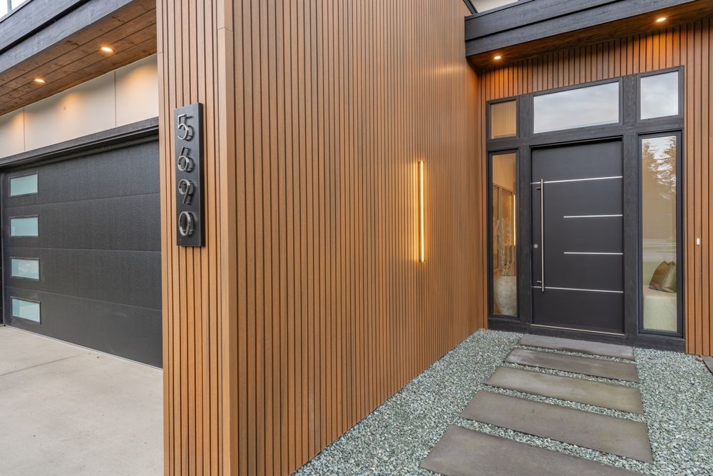 Modern house entrance with wood slat wall, glass front door, garage, and stone walkway at dusk