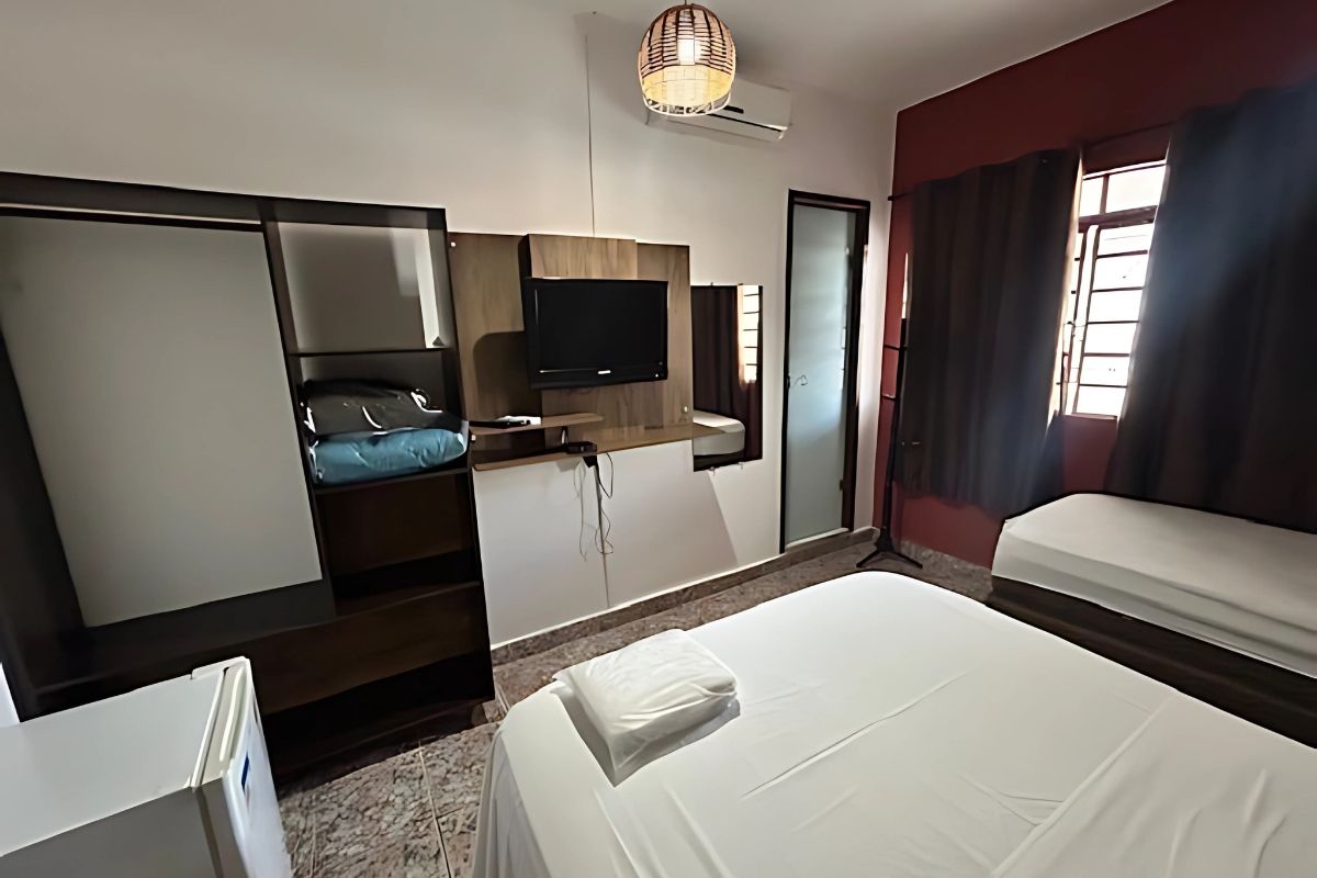Um quarto de hotel com cama, televisão, cômoda e geladeira.