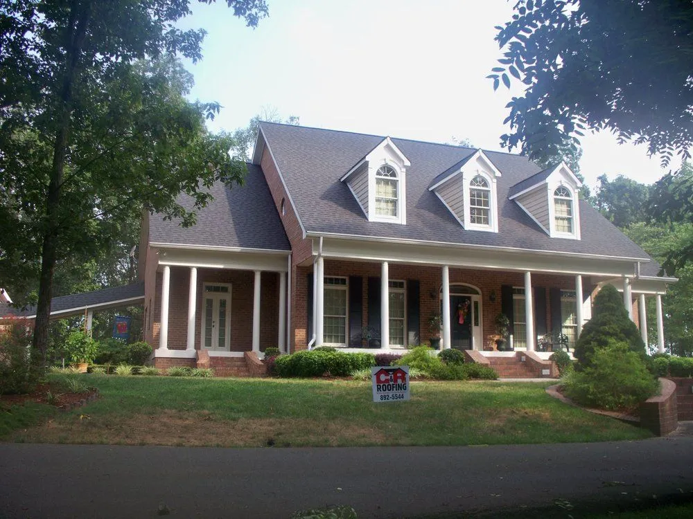Brick house with porch and dormers, on a green lawn with trees.