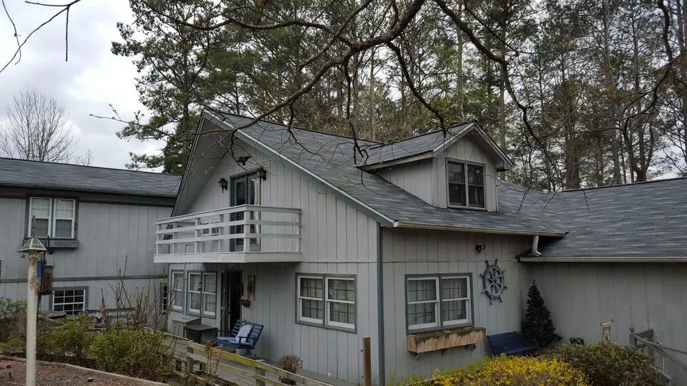 Gray house with white balcony, windows, and nautical emblem. Overhanging tree branches.