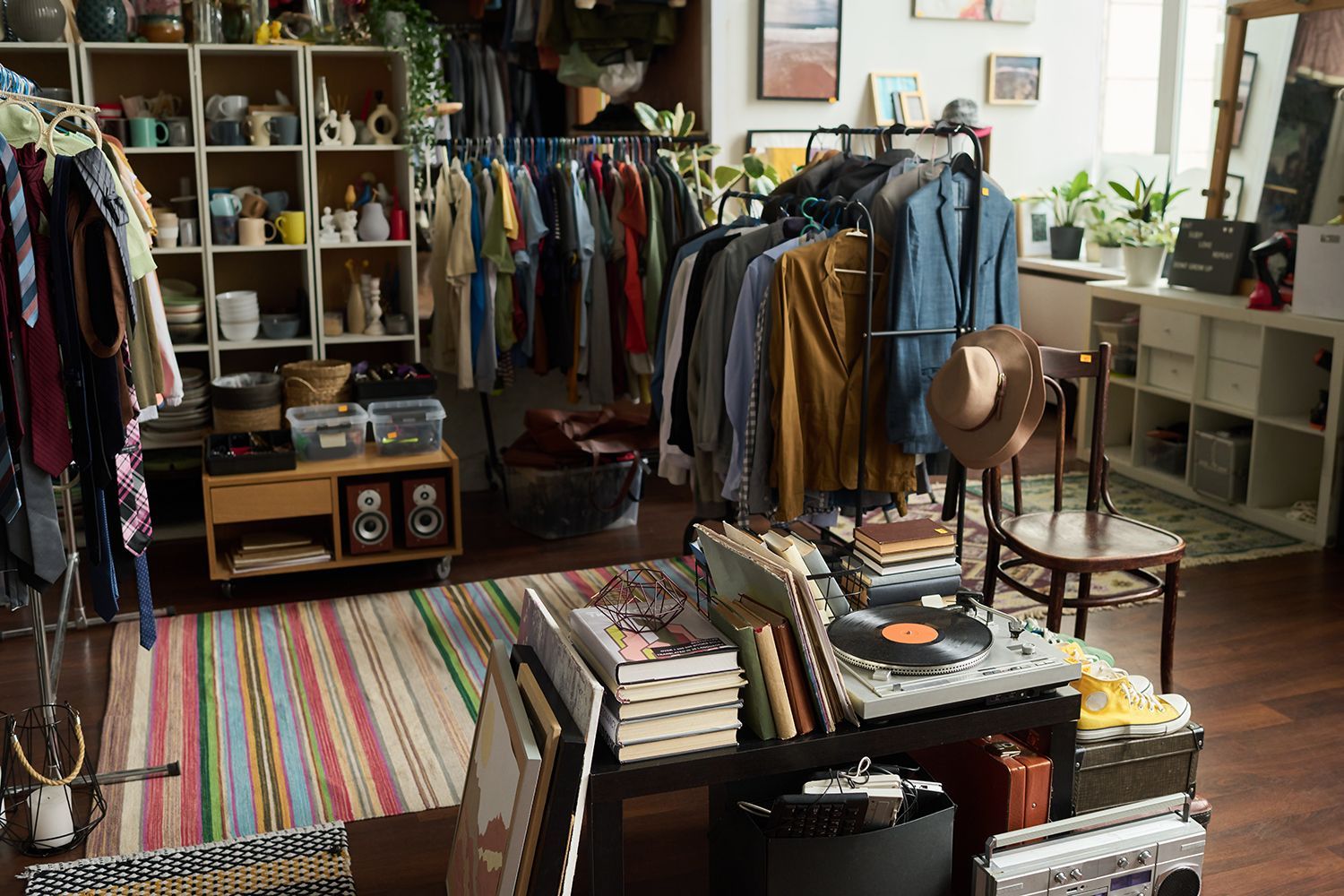 Clothing boutique with racks of colorful clothes, shelves, books, a striped rug, and chairs in a cozy room