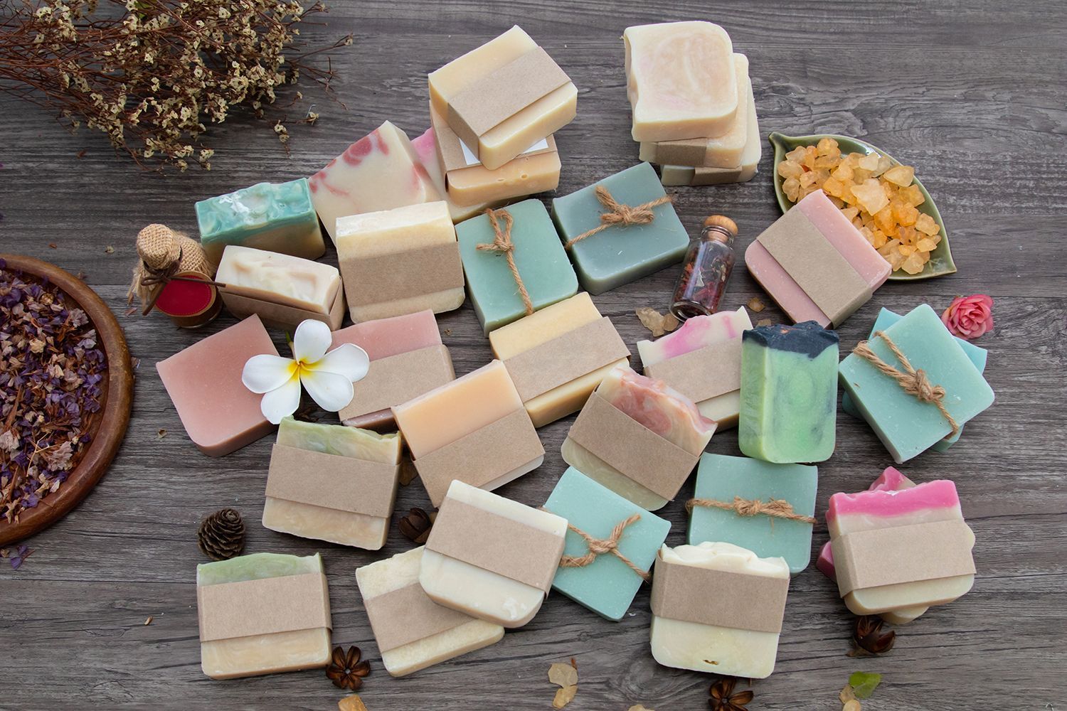 Assorted pastel handmade soap bars scattered on a wooden surface with flowers and dried petals