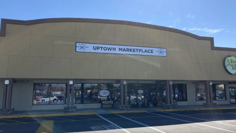 Strip mall storefront with a sign reading “Uptown Marketplace” above dark windows and parked cars. Strip mall storefront with a sign reading “Uptown Marketplace” above dark windows and parked cars.