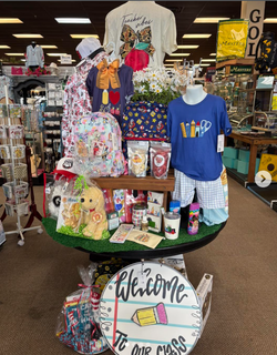 Colorful craft fair display with painted shirts, mugs, gifts, and a “Welcome to the Class” sign Colorful craft fair display with painted shirts, mugs, gifts, and a “Welcome to the Class” sign