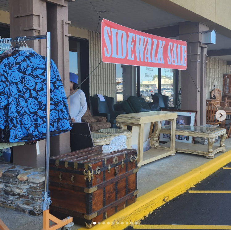 Sidewalk sale booth with vintage trunks and wooden items under a pink sale banner outside a storefront Sidewalk sale booth with vintage trunks and wooden items under a pink sale banner outside a storefront