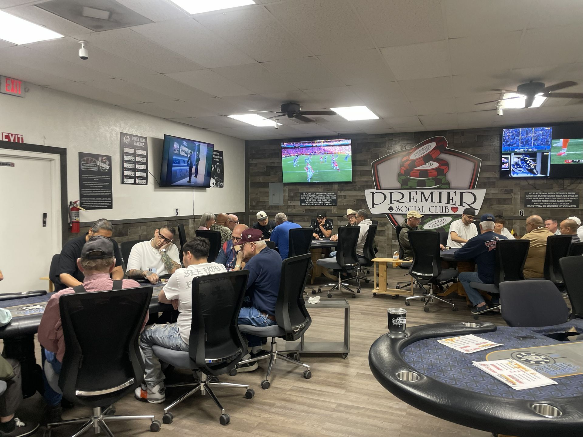 Poker room with people sitting at tables, watching TVs, playing cards.