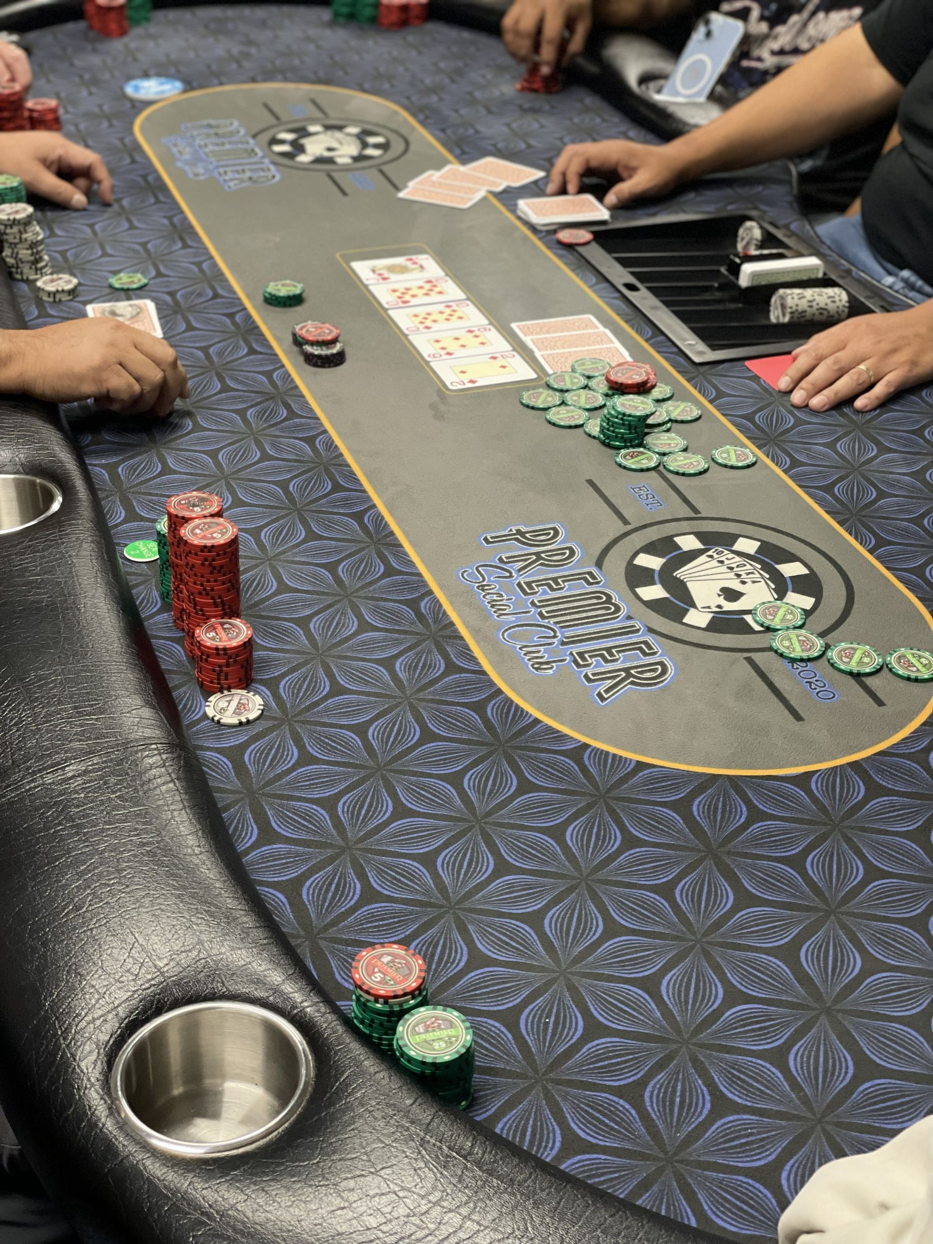 Poker table with chips and cards. Players' hands visible, reaching toward the center.