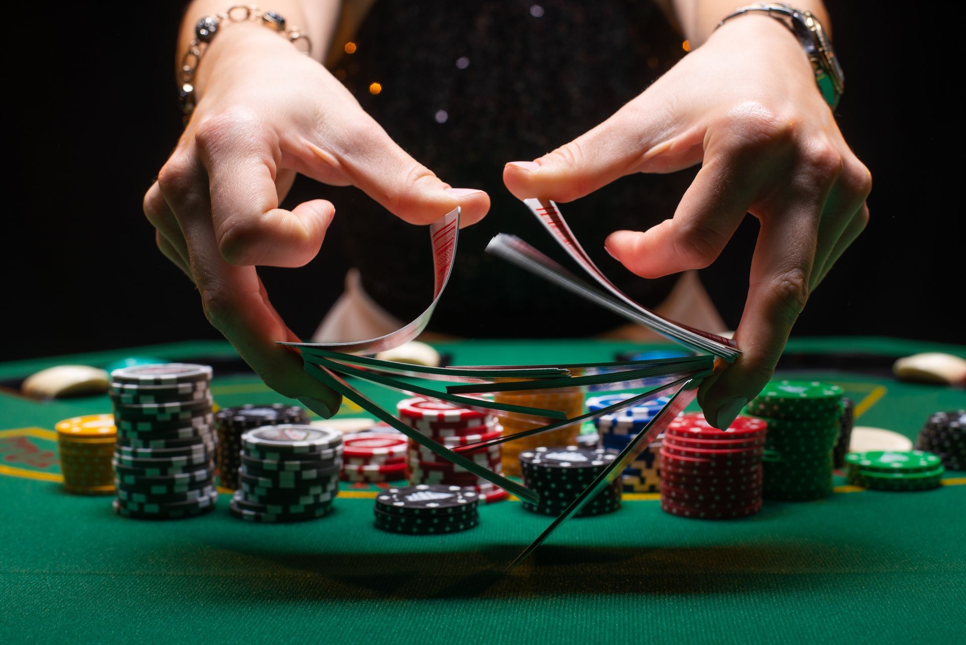 Hands holding playing cards, fanning them over a tower of poker chips on a green felt table.